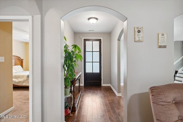 doorway with arched walkways, baseboards, hardwood / wood-style floors, and stairway