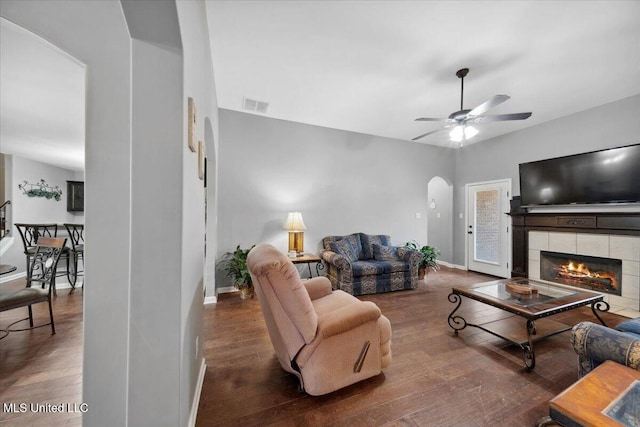 living room featuring arched walkways, wood finished floors, baseboards, a ceiling fan, and a fireplace