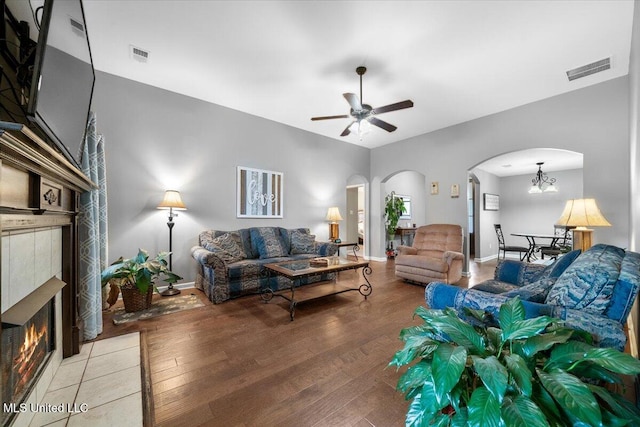 living room with arched walkways, hardwood / wood-style flooring, ceiling fan, a fireplace, and a chandelier