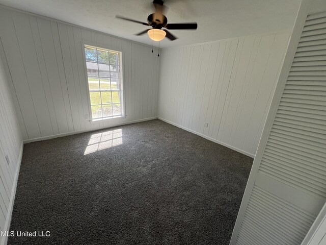 carpeted empty room featuring wooden walls and ceiling fan