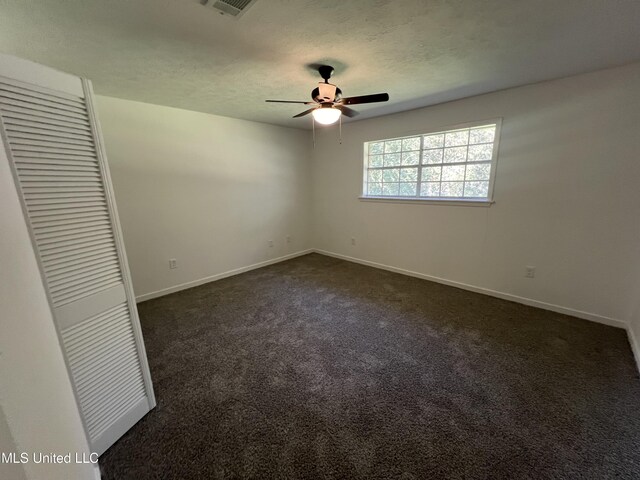 unfurnished bedroom with dark colored carpet, a closet, and ceiling fan