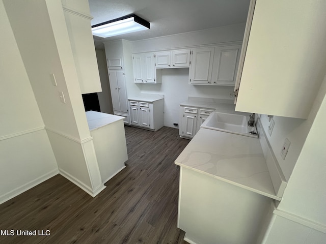 kitchen featuring light stone counters, white cabinetry, sink, and dark wood-type flooring