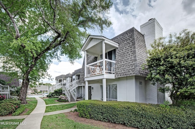 exterior space featuring stairs, a chimney, mansard roof, a balcony, and a shingled roof