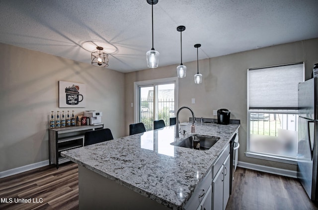 kitchen featuring freestanding refrigerator, a sink, decorative light fixtures, and dark wood-style floors