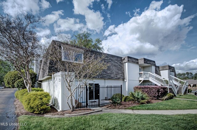 view of front of home with fence, mansard roof, a front lawn, stucco siding, and a shingled roof