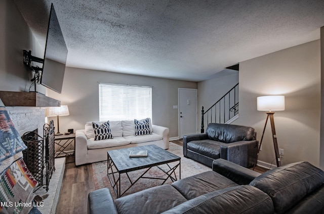 living room with stairs, a fireplace with raised hearth, baseboards, a textured ceiling, and wood finished floors