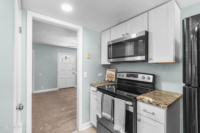 kitchen with white cabinets, light carpet, dark stone countertops, stainless steel appliances, and baseboards