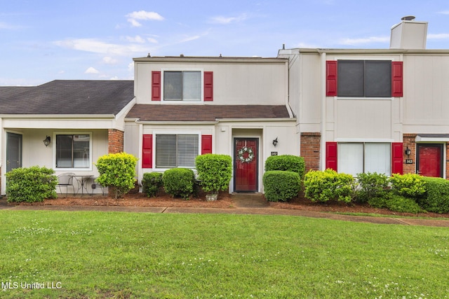 townhome / multi-family property with a shingled roof, a chimney, brick siding, and a front yard
