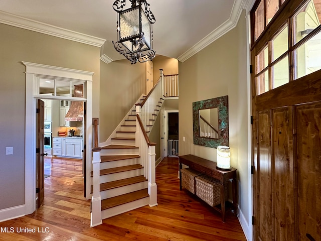 stairway featuring a notable chandelier, ornamental molding, and wood-type flooring