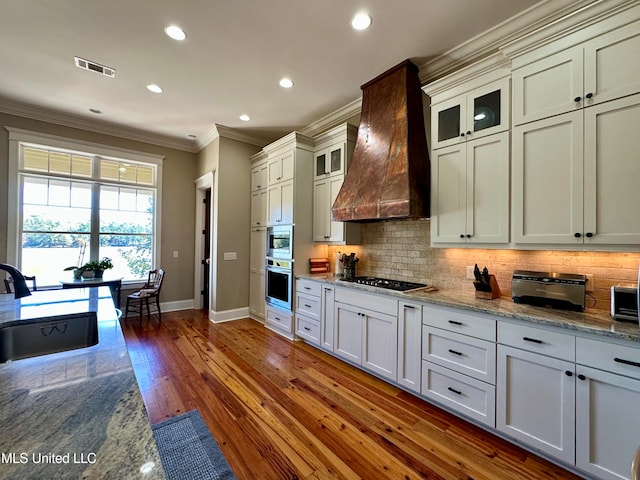 kitchen with light stone counters, premium range hood, dark hardwood / wood-style floors, sink, and stainless steel appliances