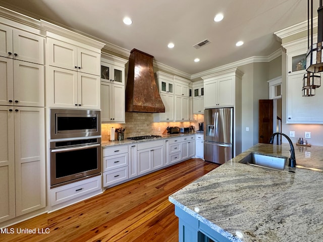 kitchen featuring hanging light fixtures, appliances with stainless steel finishes, premium range hood, dark wood-type flooring, and sink