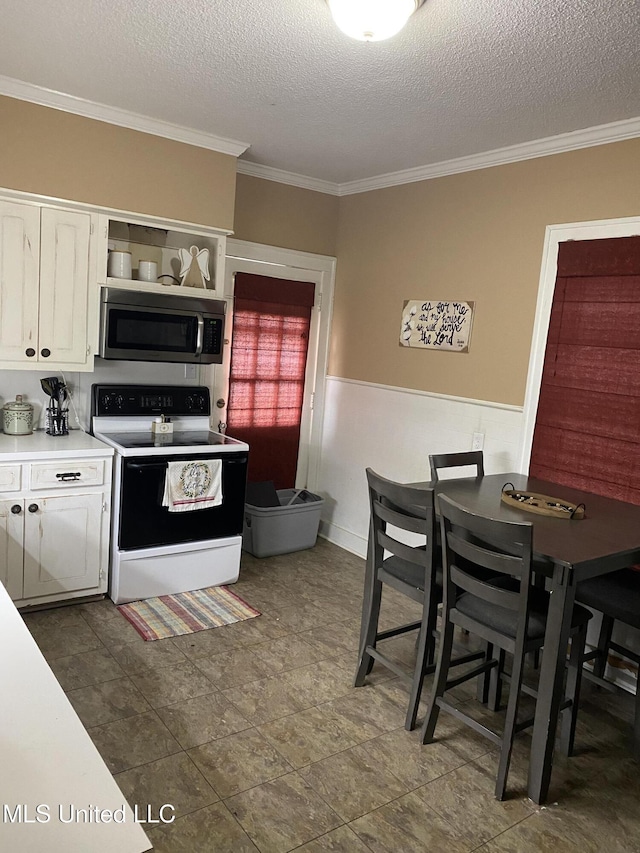 kitchen with white electric range, a textured ceiling, white cabinetry, and ornamental molding