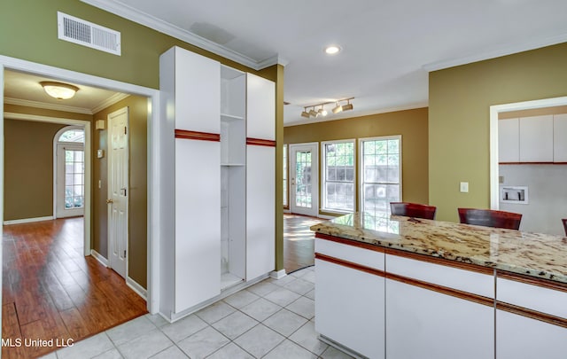 kitchen featuring a kitchen bar, light stone counters, white cabinets, crown molding, and light hardwood / wood-style flooring