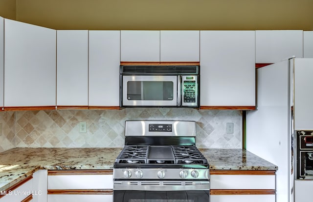 kitchen with white cabinets, light stone counters, stainless steel appliances, and tasteful backsplash