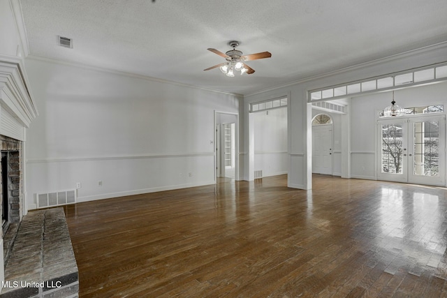 unfurnished living room with a textured ceiling, crown molding, a fireplace, and french doors