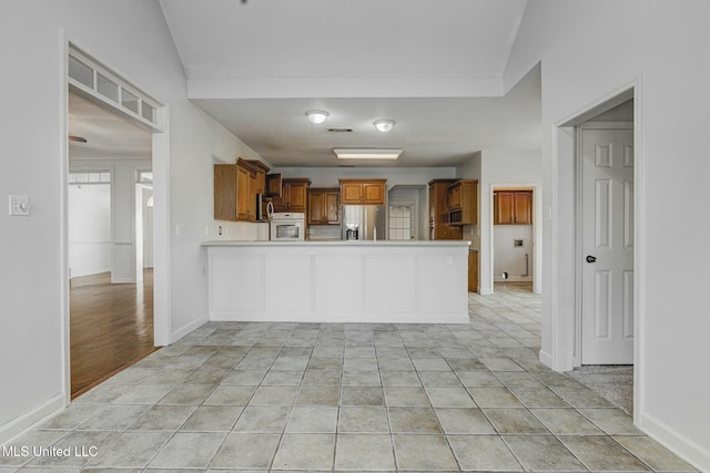 kitchen with kitchen peninsula, lofted ceiling, stainless steel appliances, and light tile patterned flooring