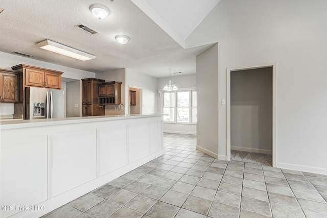 kitchen featuring light tile patterned floors, stainless steel fridge, hanging light fixtures, a textured ceiling, and a chandelier