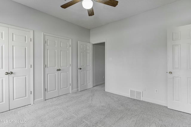 unfurnished bedroom with ceiling fan, two closets, and light colored carpet