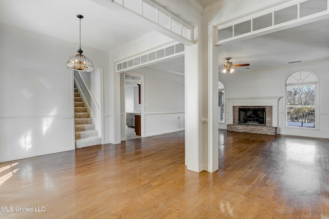 unfurnished living room with a brick fireplace, ornamental molding, and ceiling fan with notable chandelier