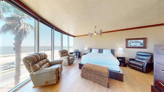 bedroom with ornamental molding, a water view, a textured ceiling, light hardwood / wood-style floors, and floor to ceiling windows