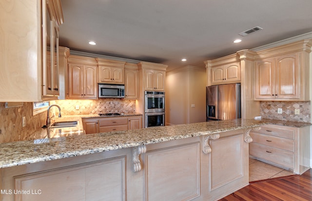 kitchen featuring light stone countertops, appliances with stainless steel finishes, light brown cabinetry, and light hardwood / wood-style floors