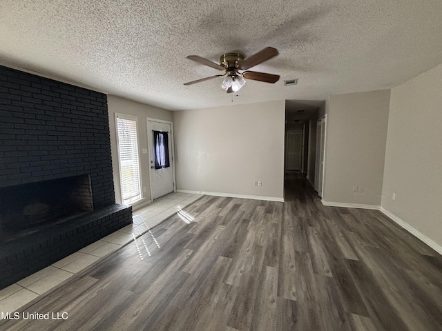 unfurnished living room with a brick fireplace, wood-type flooring, a textured ceiling, and ceiling fan