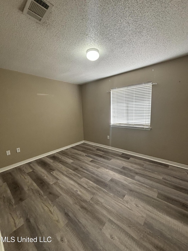 empty room featuring dark wood finished floors, baseboards, visible vents, and a textured ceiling