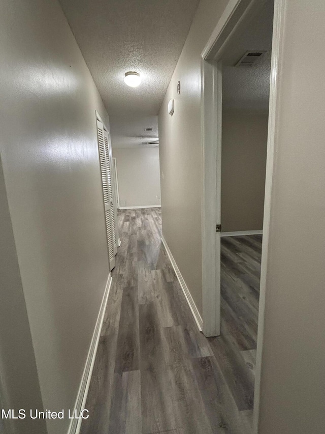 corridor featuring wood finished floors, a textured ceiling, baseboards, and visible vents