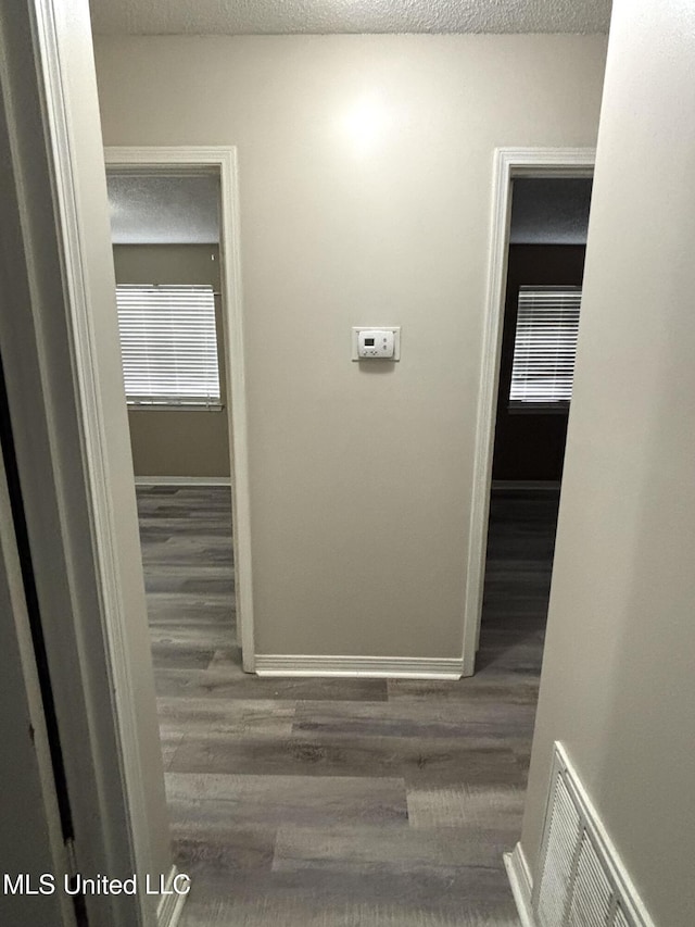corridor featuring baseboards, wood finished floors, visible vents, and a textured ceiling