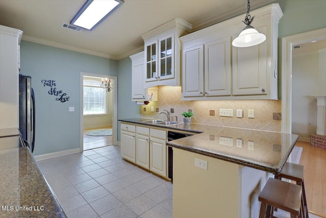 kitchen with a sink, visible vents, a kitchen breakfast bar, ornamental molding, and dishwasher