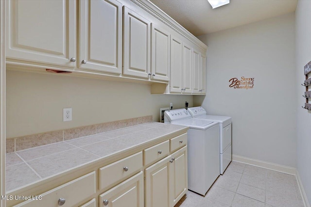 clothes washing area featuring light tile patterned floors, cabinet space, baseboards, and separate washer and dryer