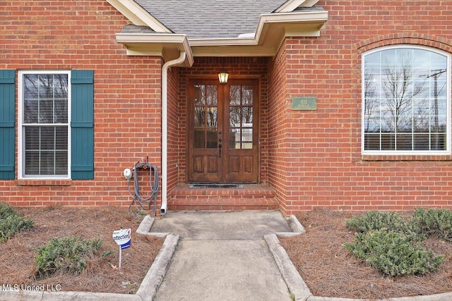 property entrance featuring french doors, a shingled roof, and brick siding