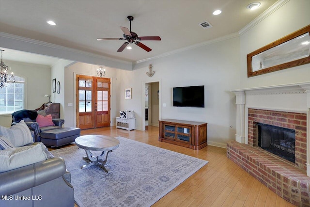 living area with visible vents, ornamental molding, french doors, light wood-type flooring, and a brick fireplace