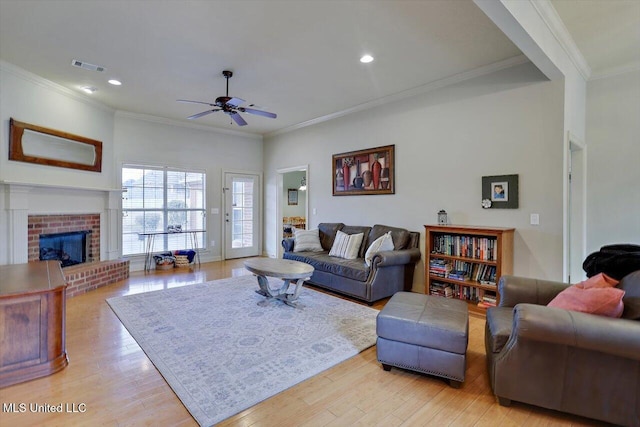 living room with crown molding, light wood-type flooring, visible vents, and a brick fireplace