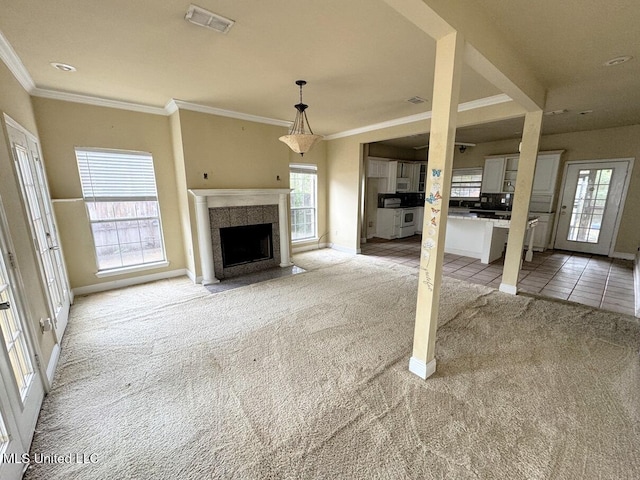 unfurnished living room featuring a tiled fireplace, crown molding, and light colored carpet