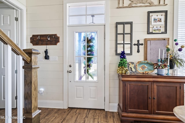 foyer entrance with stairs, wood walls, dark wood-style flooring, and baseboards