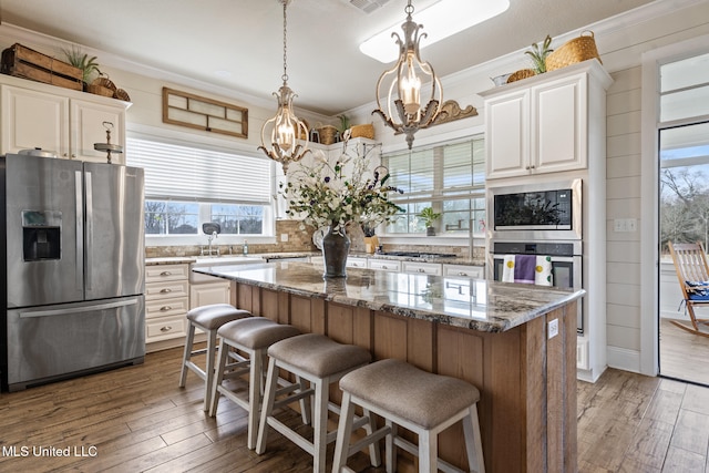 kitchen with dark stone counters, appliances with stainless steel finishes, a center island, crown molding, and white cabinetry