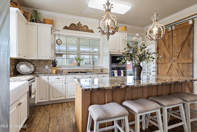 kitchen with appliances with stainless steel finishes, dark stone counters, white cabinets, and crown molding