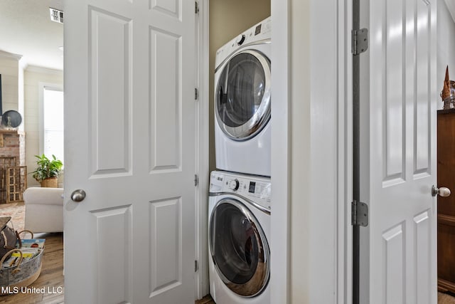 laundry area featuring crown molding, stacked washer / drying machine, visible vents, wood finished floors, and laundry area