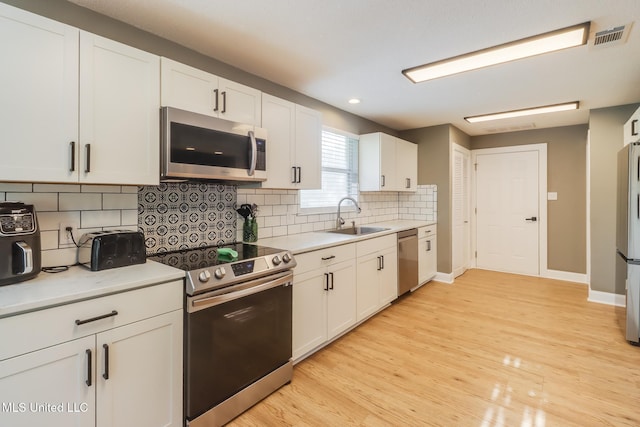 kitchen with appliances with stainless steel finishes, a sink, white cabinetry, light countertops, and recessed lighting