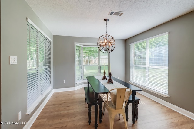 dining space featuring a chandelier, a textured ceiling, baseboards, and wood finished floors