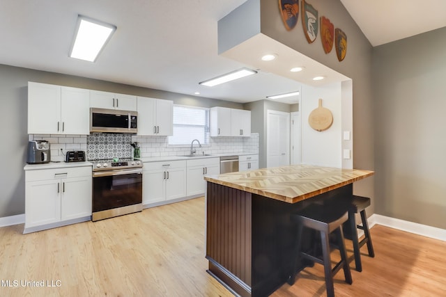 kitchen with appliances with stainless steel finishes, wood counters, decorative backsplash, baseboards, and a sink