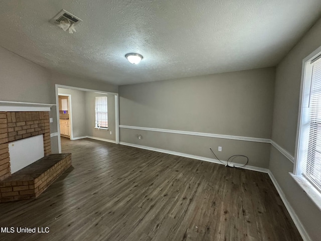 unfurnished living room with dark hardwood / wood-style flooring, a brick fireplace, and a textured ceiling