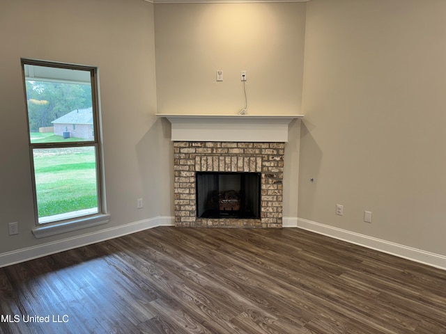 unfurnished living room with dark wood-type flooring, a healthy amount of sunlight, and a brick fireplace