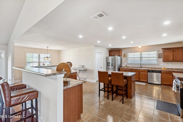 7637 Wisteria Dr, Olive Branch, MS 38654 - kitchen featuring a kitchen island, a healthy amount of sunlight, stainless steel appliances, brown cabinets, and a breakfast bar area