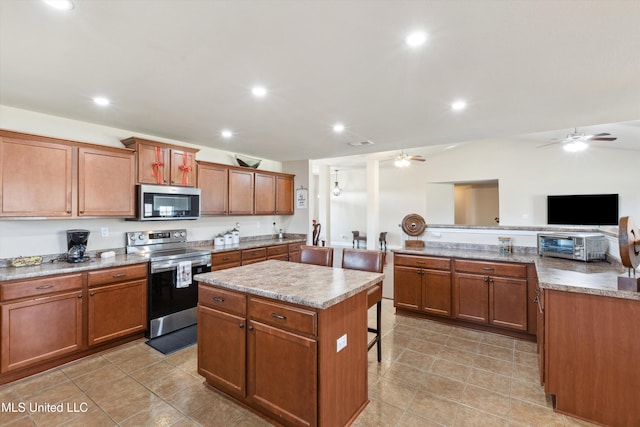 7637 Wisteria Dr, Olive Branch, MS 38654 - kitchen featuring ceiling fan, a kitchen breakfast bar, a kitchen island, appliances with stainless steel finishes, and brown cabinets