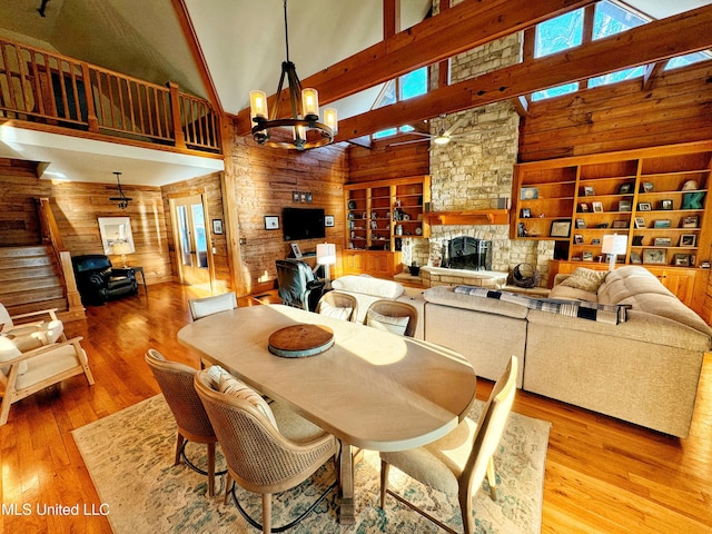 dining area featuring a towering ceiling, an inviting chandelier, a fireplace, wooden walls, and light wood-type flooring