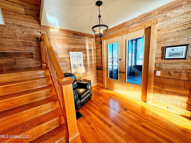 living area with french doors, hardwood / wood-style floors, a chandelier, and wood walls