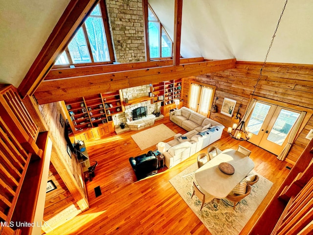 living room featuring a stone fireplace, wood-type flooring, high vaulted ceiling, and a healthy amount of sunlight