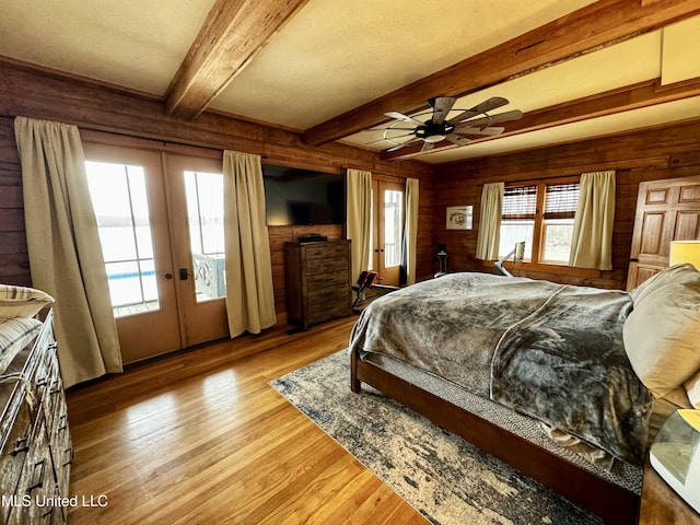 bedroom with french doors, wooden walls, ceiling fan, beam ceiling, and light hardwood / wood-style floors